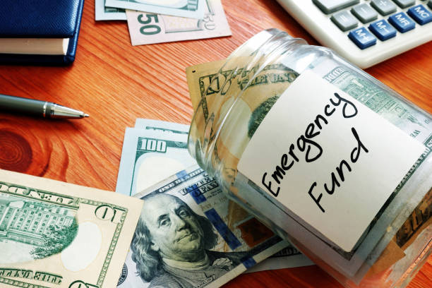 An emergency fund jar tipped on its side, filled with money, with additional bills scattered around it.