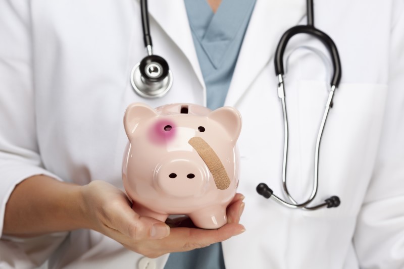 A doctor with a stethoscope holding a piggy bank with bruises and a bandage, symbolizing the importance of financial check-ups.