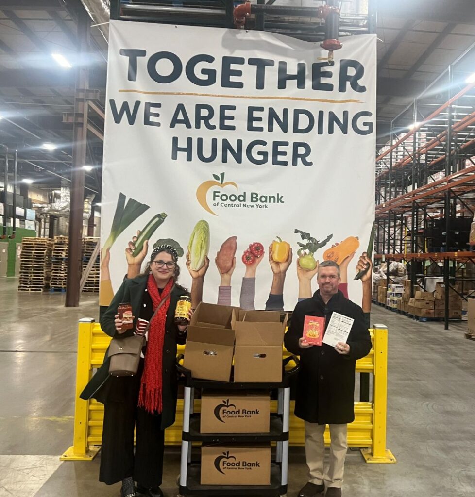 Taylor and Pat from HighPoint Advisors, LLC at the Food Bank of Central New York facility, standing next to their food drive box donations