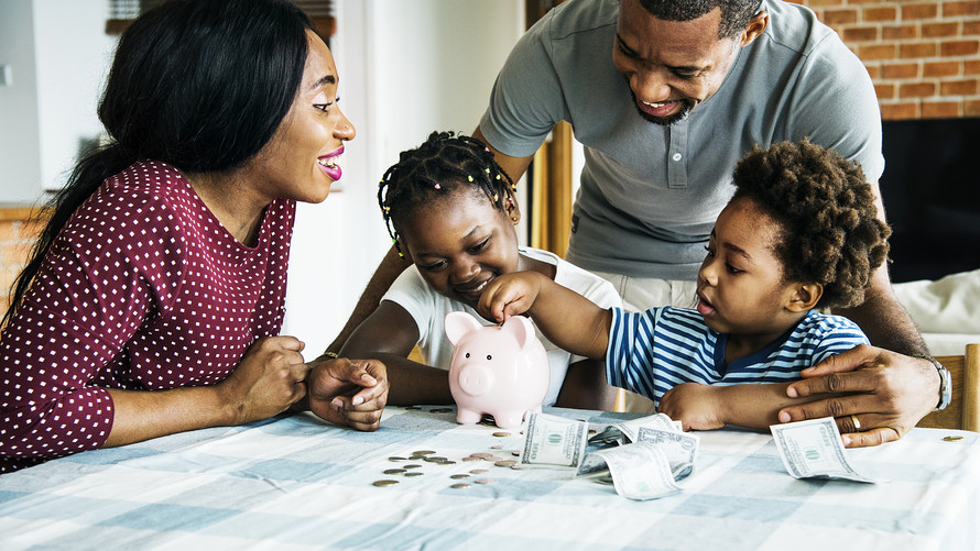 A family with parents and children inserting money into a piggy bank surrounded by scattered bills and coins.